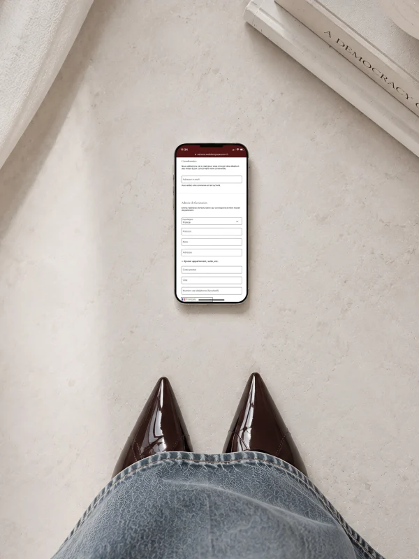 Sur une table, un smartphone affiche un formulaire d'adresse de livraison avec des champs pour l'e-mail, l'adresse et le numéro de téléphone.